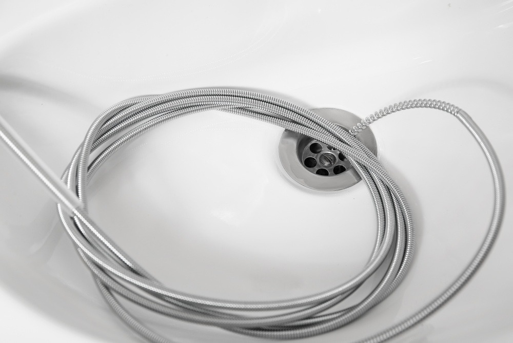 A drain snake going down a bathtub drain.