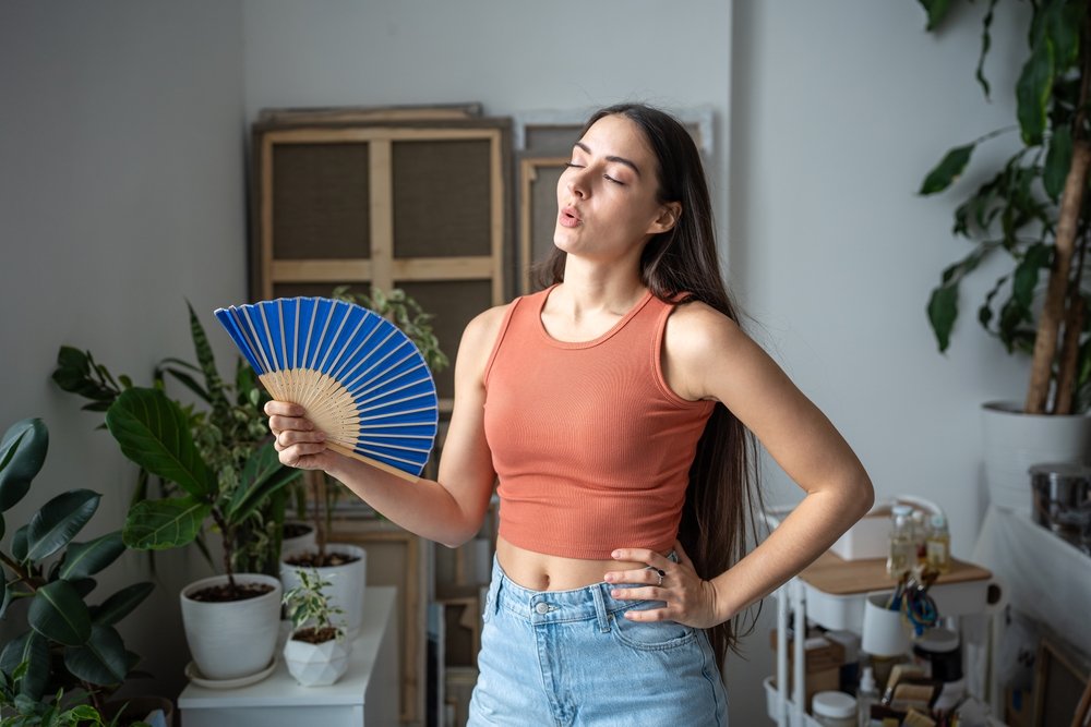 A woman fanning herself indoors.